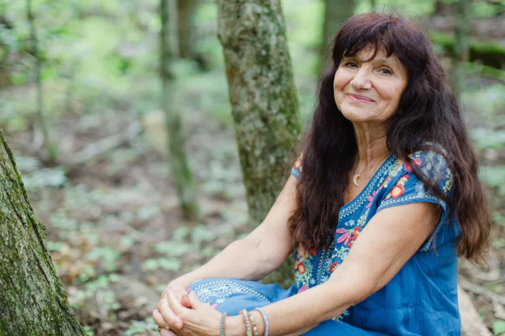 Smiling woman sitting peacefully in a forest, enjoying nature.